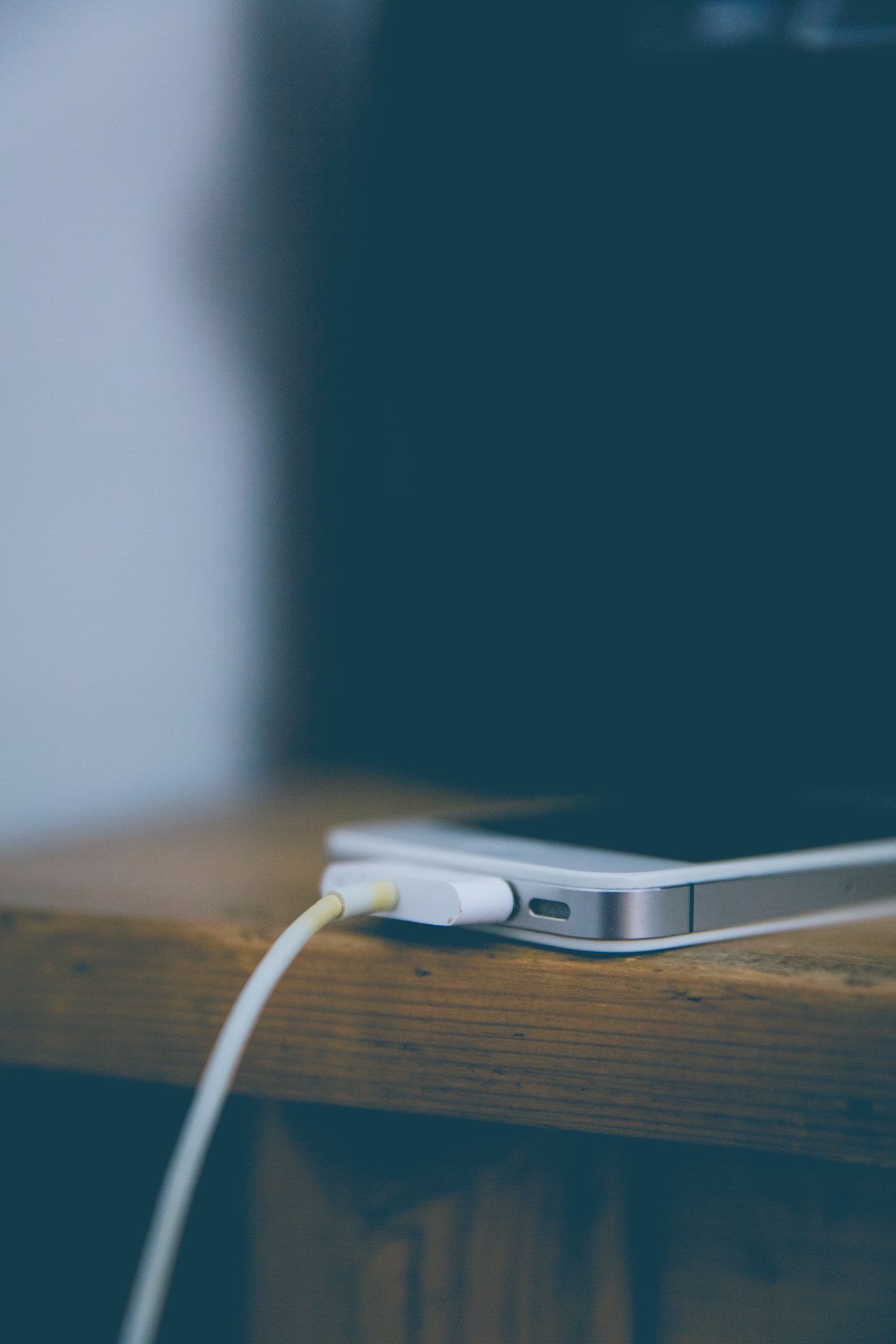 Telefon disambungkan pada kabel pengecas di atas meja kayu