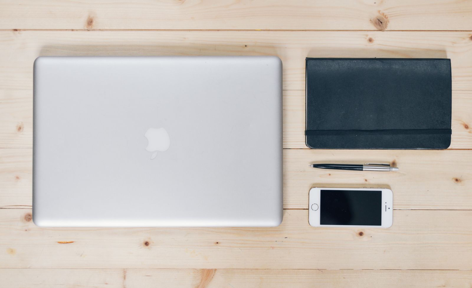 MacBook ditutup bersama telefon dan buku nota di atas meja