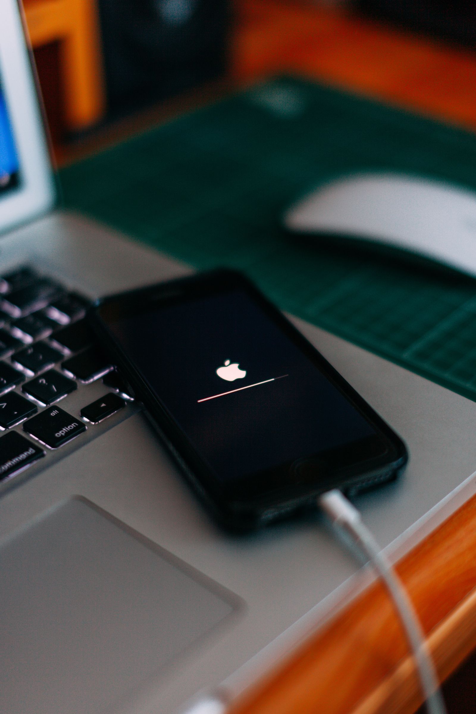 iPhone dengan kabel pengecas berdekatan komputer riba